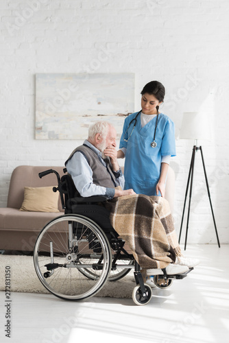 Nurse standing near tired and disabled senior man in wheelchair
