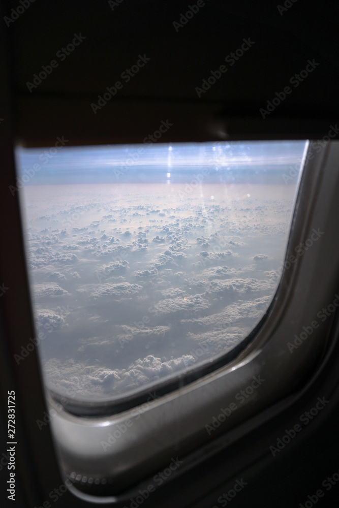 Airplane window overlooking the beautiful clouds and the earth. Sunset in flight on vacation. Tourist theme. Stock photo