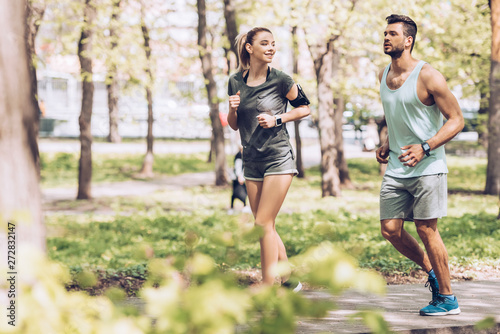 selective focus of smiling woman and handsome man jogging in park