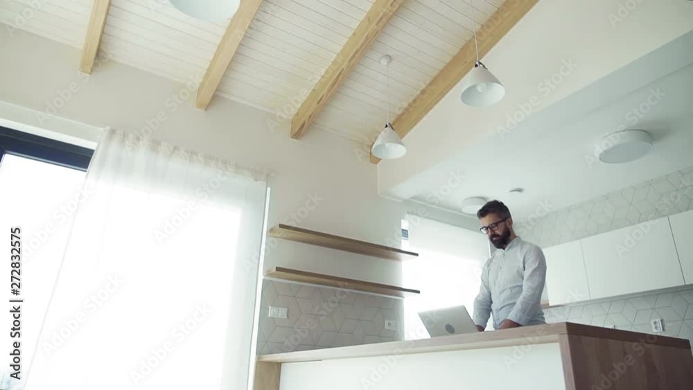 A mature man with laptop standing in kitchen in unfurnished new house. A mature man with laptop standing in kitchen in unfurnished new house.