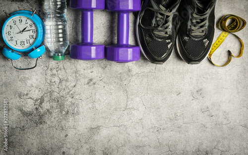 Sport shoes, blue alarm clock, bottle of water and centimeter on grunge cement background background. Sport equipment. Concept healthy life.