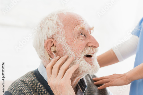 Profile of happy and cheerful man with hearing aid in ear, looking away photo