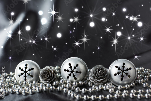 Three silver jingle bells, two silver cones and bead chain on grey cloth background - taxt space