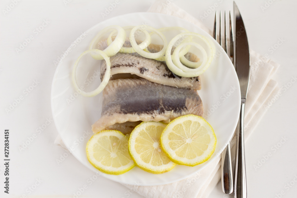 delicious tender herring fillet with lemon and onion on white plate on white background delicious tender herring fillet with lemon and onion on white plate on white background