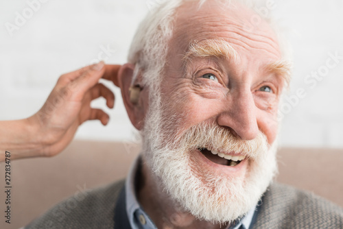 Woman hand helping grey haired man, wearing hearing aid