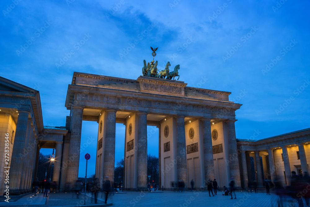 Obraz premium Many tourists hanging out at the famous and illuminated neoclassical Brandenburg Gate (Brandenburger Tor) in Berlin, Germany, at dusk.