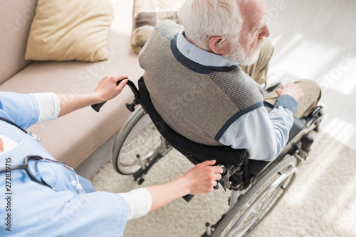 High angle view of nurse standing behind disabled gray haired man in wheelchair
