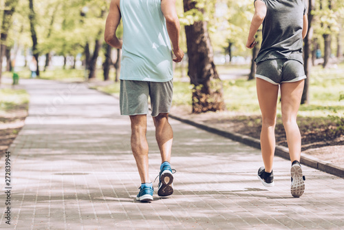 cropped shot of man in woman jogging together along walkway in park