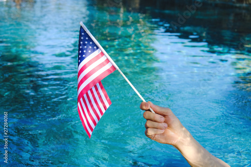 Hand waving American flag with blue pool water in background.  Fourth of July holiday celebration concept. photo