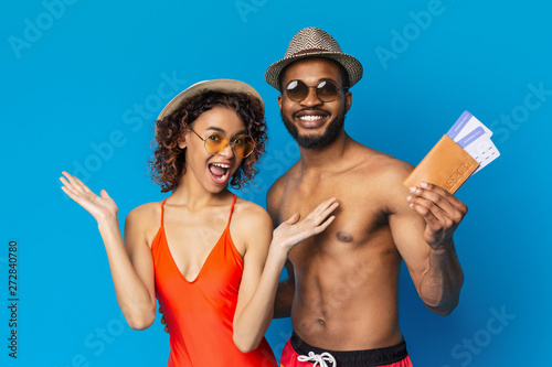 Happy african couple in swimsuits ready to chill out with tickets to resort