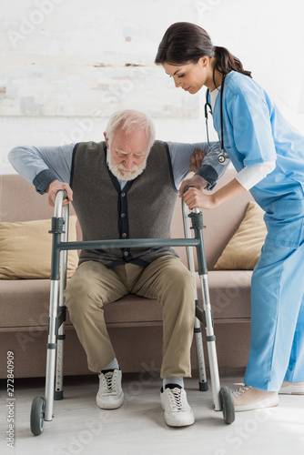 Bild auf Leinwand Nurse helping to retired man, getting up from sofa