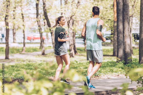 Fototapeta Naklejka Na Ścianę i Meble -  young man and woman talking while jogging together in sunny park