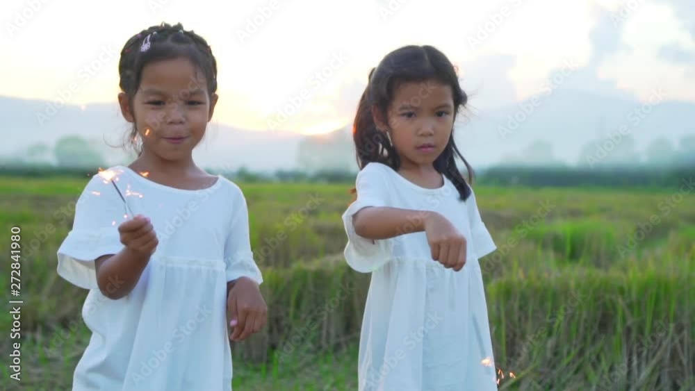 Happy kids standing and dancing with burning sparkles in field at the evening time. Celebrating with sparklers in the twilight in Slow motion. Happy kids standing and dancing with burning sparkles in field at the evening time. Celebrating with sparklers in the twilight in Slow motion.