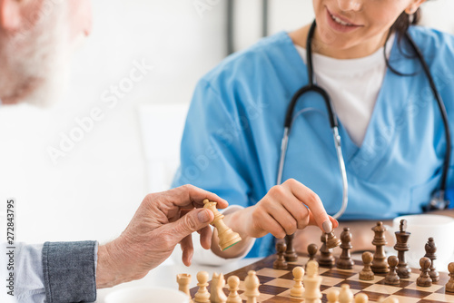 Cropped view of nurse and senior man sitting on kitchen, and playing in chess