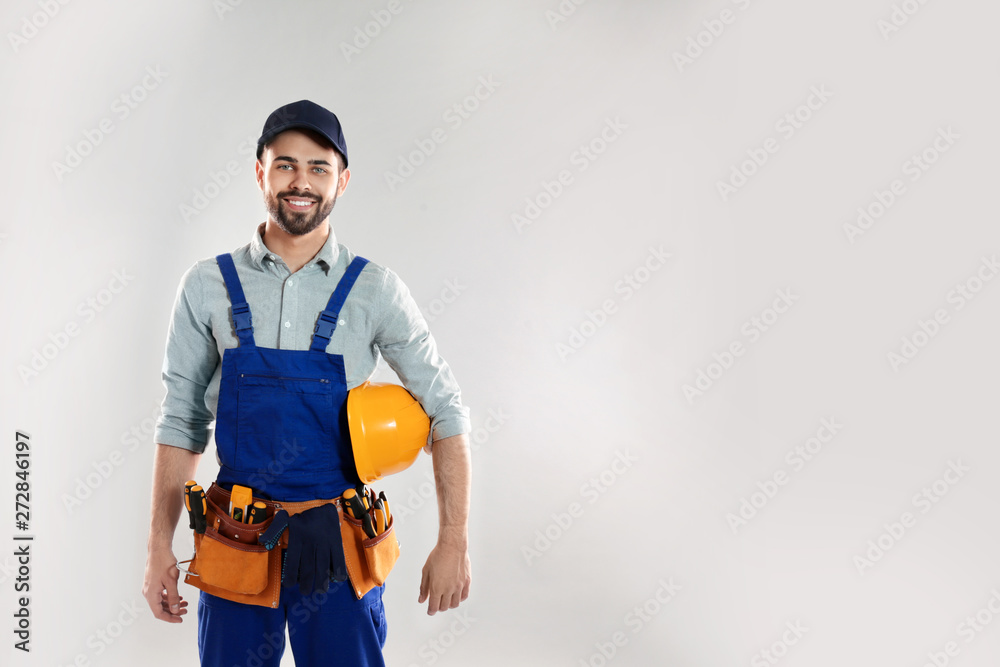 Portrait of construction worker with hard hat and tool belt on light background, space for text - obrazy, fototapety, plakaty 