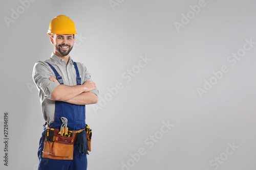 Portrait of professional construction worker with tool belt on grey background, space for text