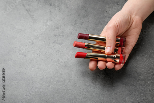 Woman holding different lipsticks on color background  closeup with space for text. Professional makeup products