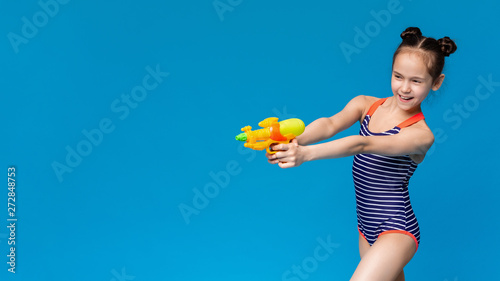 Cheerful girl in swimwear shooting aside with water gun