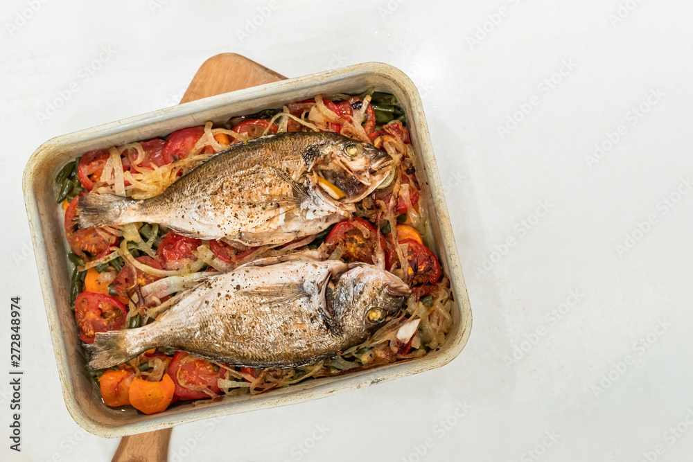 Fish, cooked on vegetable cushion in metal baking tray on white background. Fish, cooked on vegetable cushion in metal baking tray on white background.