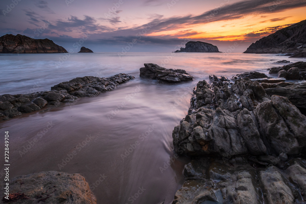 Obraz premium Colorful cloudy Sunrise at the beach of playa de la arnia with dynamic waves and bizarre rocks, Liencres, Northern Spain