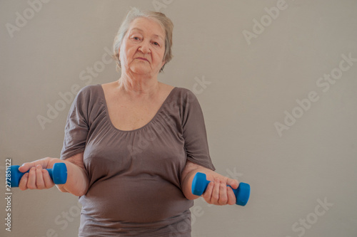  Health-conscious. Charming upbeat elderly lady working out with dumbbells and smiling pleasantly at the camera at home.