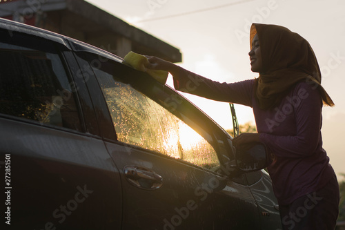 hijab Woman car washing with yellow sponge  washing her car  in front of the house photo