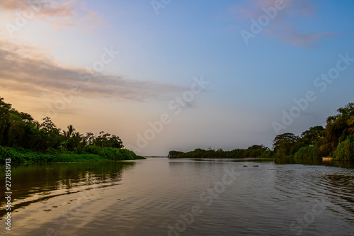 A wide, shallow river flows calmly through the deep South American jungle at blue violet dusk