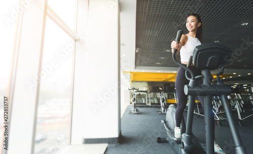 Girl exercising on elliptical trainer in gym