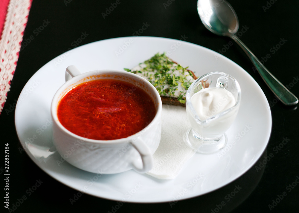 Borsch in a plate on a black table. Near bread with bacon, spoon, napkin and sour cream. Borsch in a plate on a black table. Near bread with bacon, spoon, napkin and sour cream.