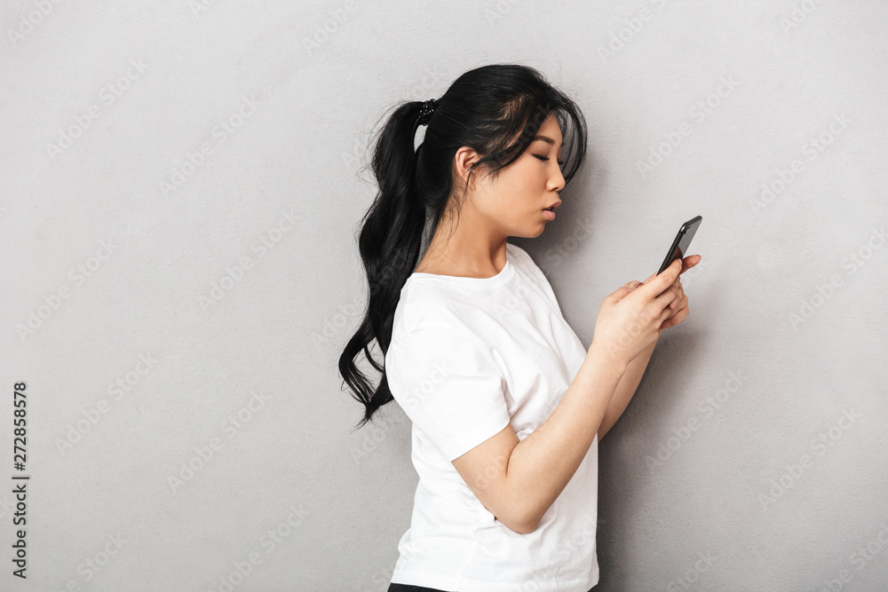Asian beautiful young woman posing isolated over grey wall background using mobile phone. Asian beautiful young woman posing isolated over grey wall background using mobile phone.