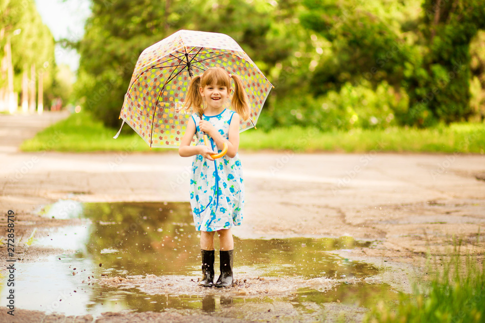 happy child girl in dress with an umbrella and rubber boots in puddle on summer walk