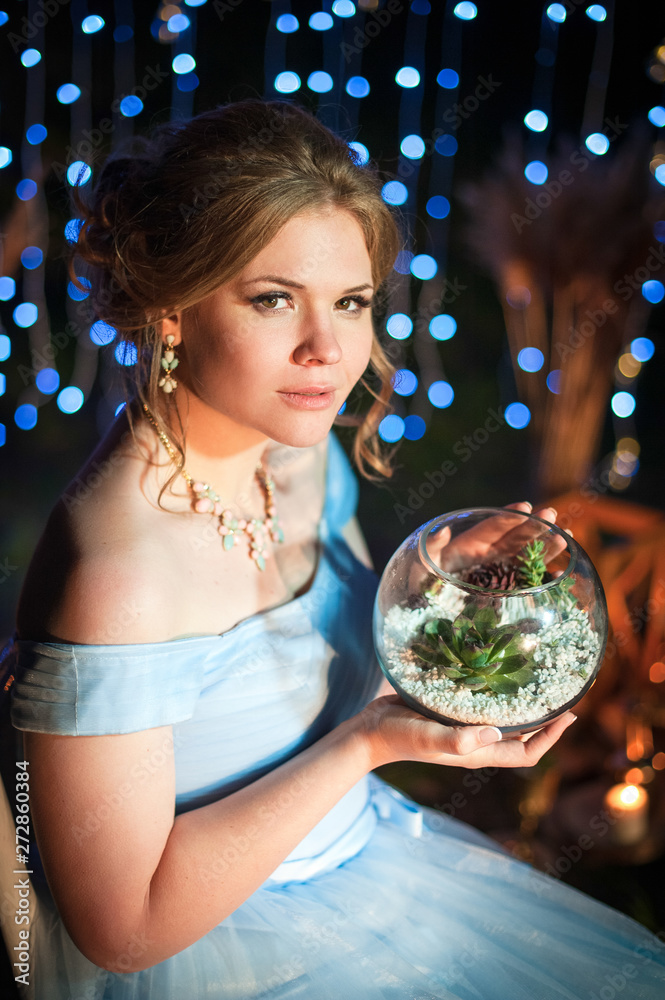 Naklejka premium young beautiful girl holding a vase with succulent plants on a dark background with lights 