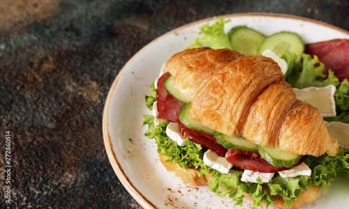 croissant sandwich and tea. breakfast in French. jerky, camembert cheese, lettuce, cucumber, croissant. copy space. 