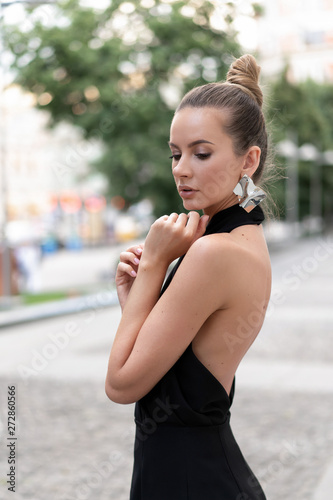 Young slim girl in black dress posing on the street near the white wall. In the ears of the original metal earrings. Very stylish and beautiful model.