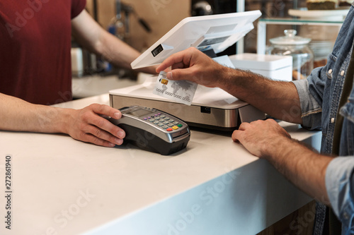 Fototapeta Cropped photo of caucasian man paying debit card in cafe while waiter holding pa