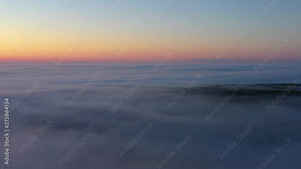 Sliding high above a fog bank with a forest peaking though during a pink sunrise AERIAL Sliding high above a fog bank with a forest peaking though during a pink sunrise AERIAL