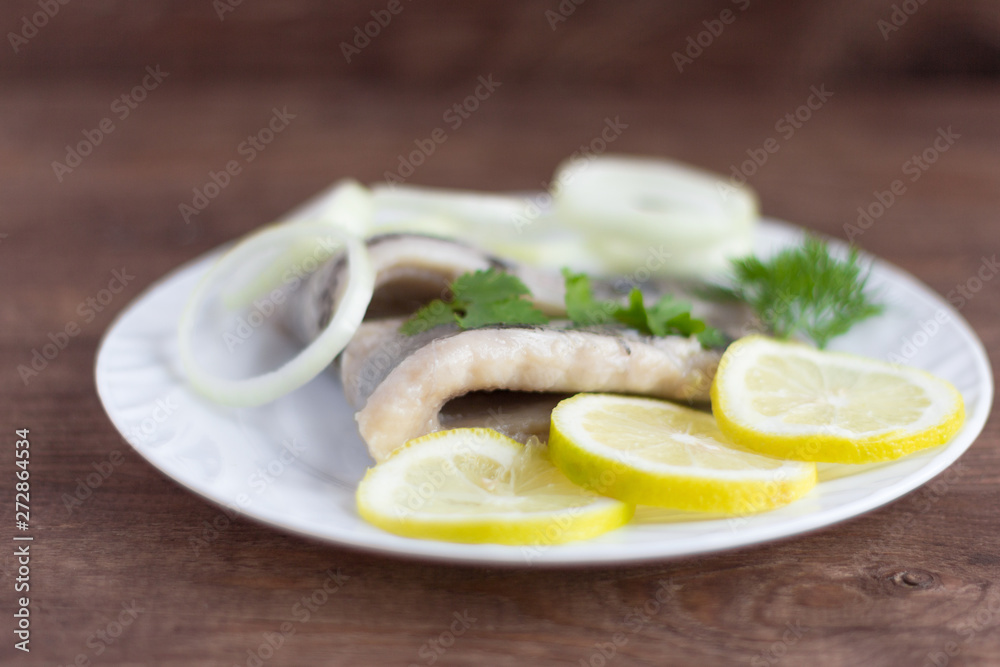 delicious tender herring fillet with lemon,herbs and onion on white plate on wooden background