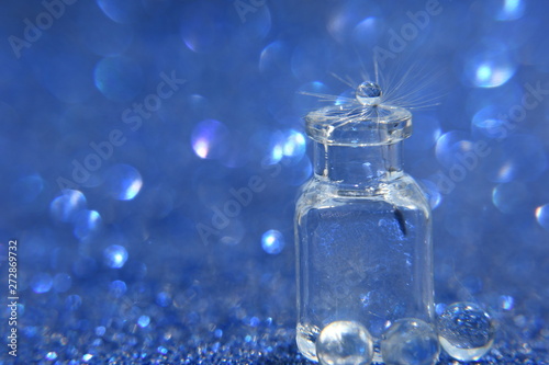 Dandelion seed with drop of water in glass bottle on blue bokeh background. An artistic picture of dandelion flower.