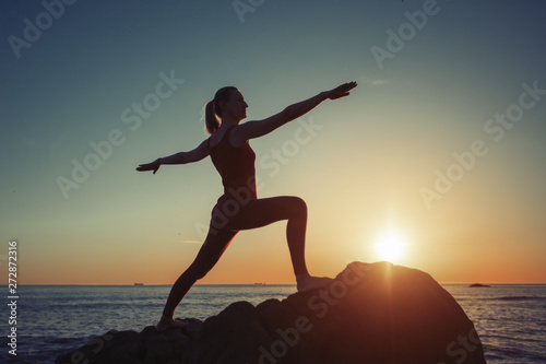 Silhouette of woman doing yoga exercises on the sea coast at sunset.