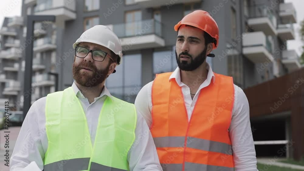 The builder and architect man are discussing the construction plan of the modern business center walking near construction site. They checks the work with architectural drafting. The builder and architect man are discussing the construction plan of the modern business center walking near construction site. They checks the work with architectural drafting.