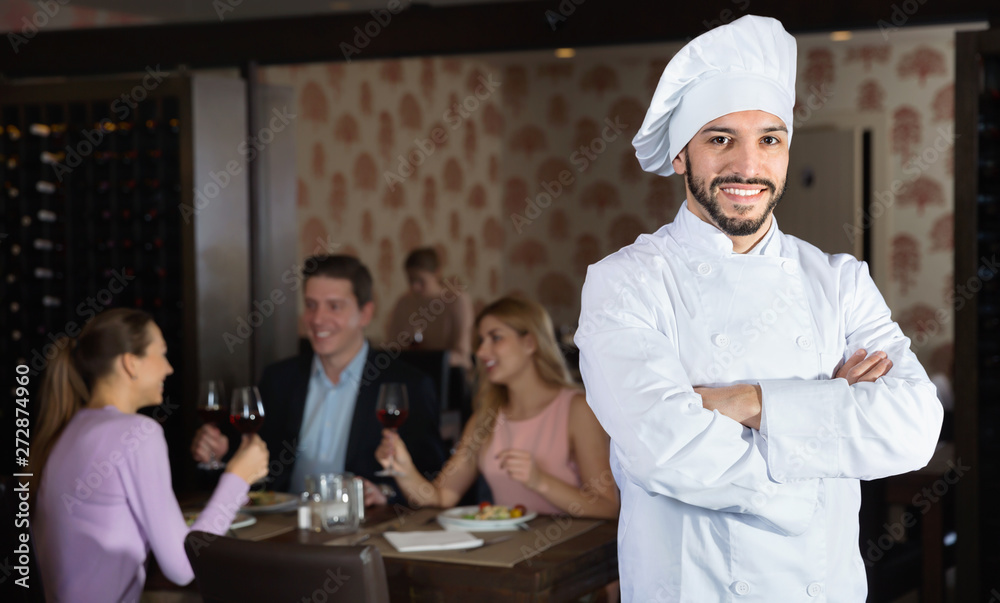 Portrait of handsome professional chef on background with restaurant guests