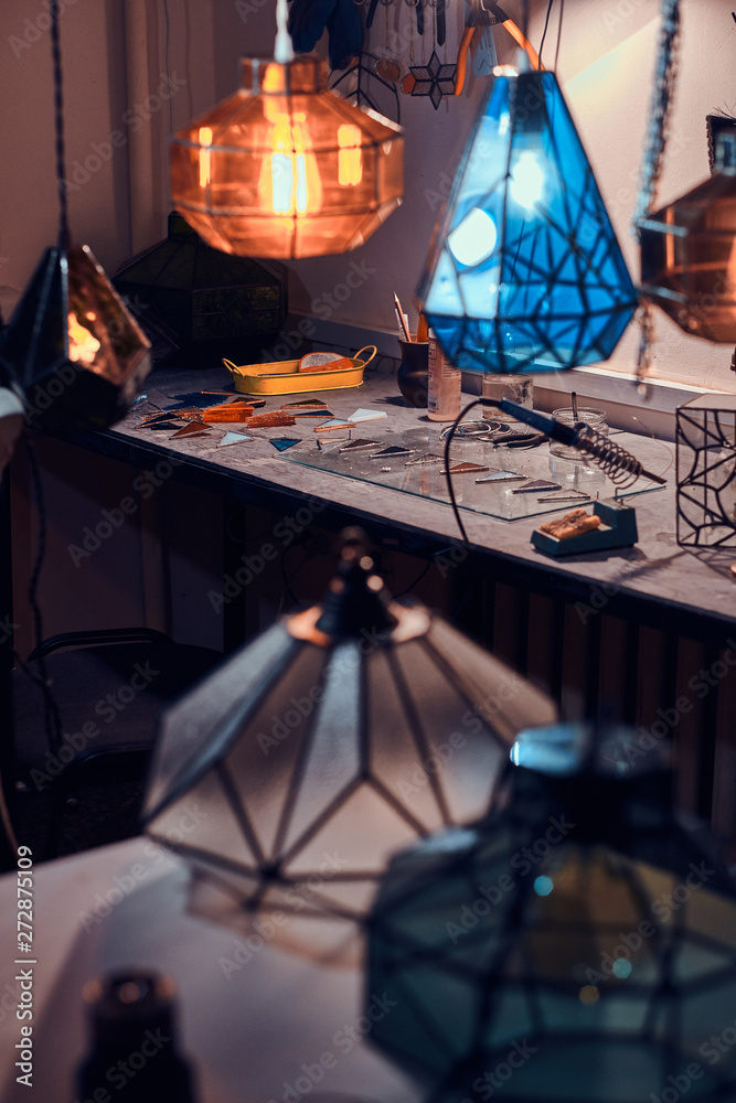 Master's workspace, table and beautiful colourful glass lamps at cozy workshop.