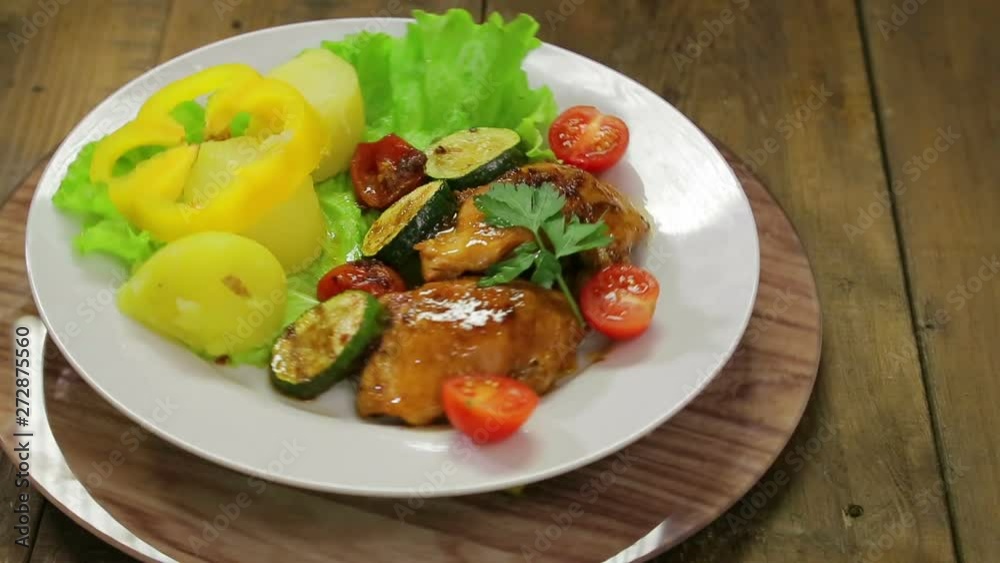 A rotating plate with a grilled chicken dish and a side dish of vegetables A rotating plate with a grilled chicken dish and a side dish of vegetables