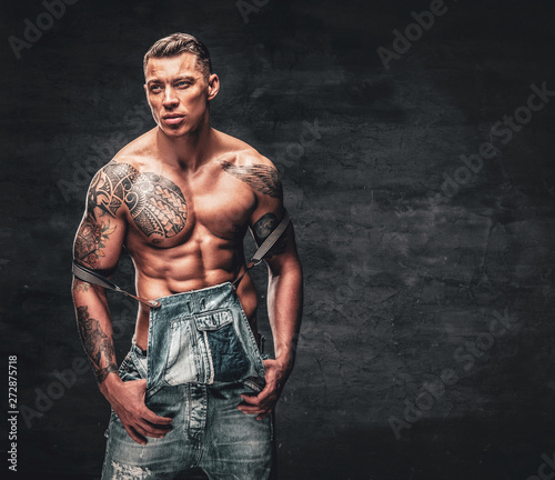 Studio portrait of handsome shirtless muscular, athletic male with a tattoo on his chest dressed in a jeans.