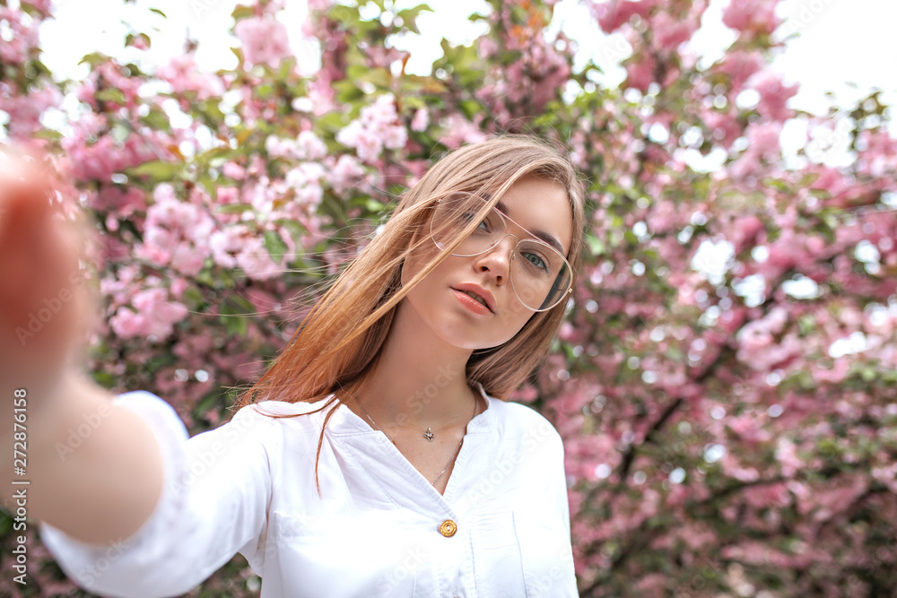 beautiful young happy woman in a blouse and glasses near the cherry blossoms. flowers beautiful young happy woman in a blouse and glasses near the cherry blossoms. flowers