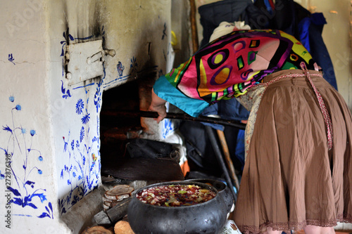 rural woman in traditional clothes putting a pot on fire into a russian stove