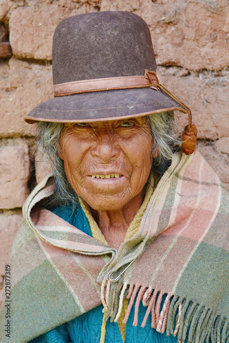 Happy old native american woman wearing typical aymara clothes. Adobe wall background.
