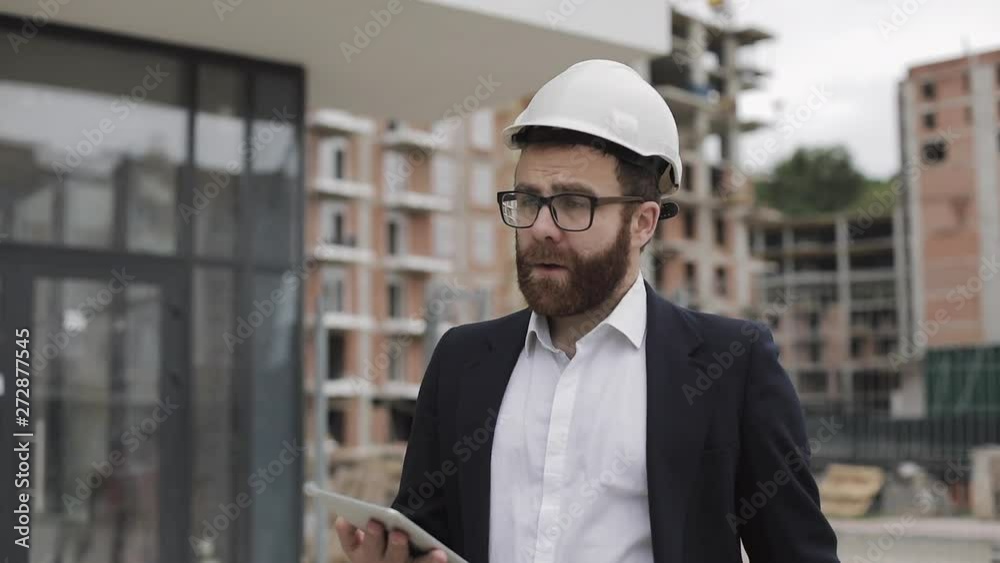 Architect man wearing business suit walking with tablet on the construction site and analyzing scheme project plan. Outside, slow motion. Architect man wearing business suit walking with tablet on the construction site and analyzing scheme project plan. Outside, slow motion.