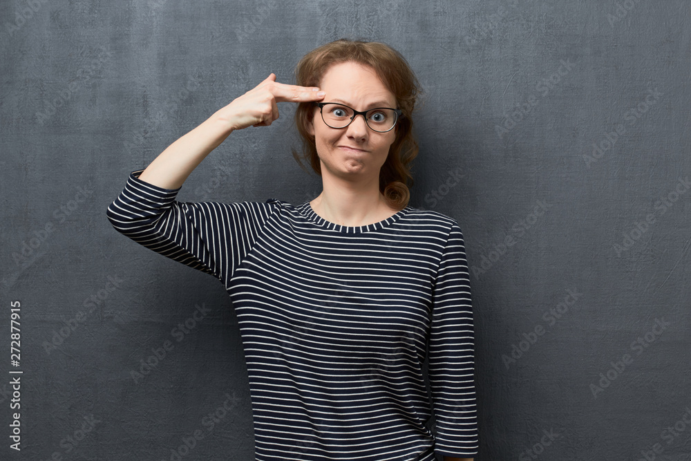 Portrait of confused woman showing gun gesture near temple