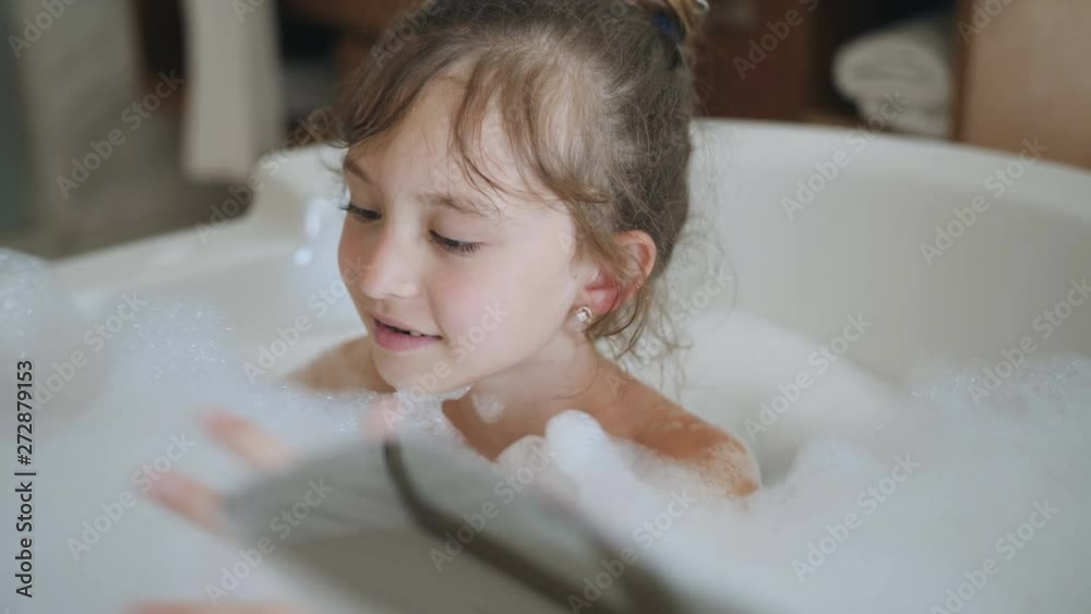 Little girl playing with shower attachment while taking the bath. Happy child girl in the shower. Positive little girl having bath with bubbles in bathtub Stock ビデオ | Adobe Stock 